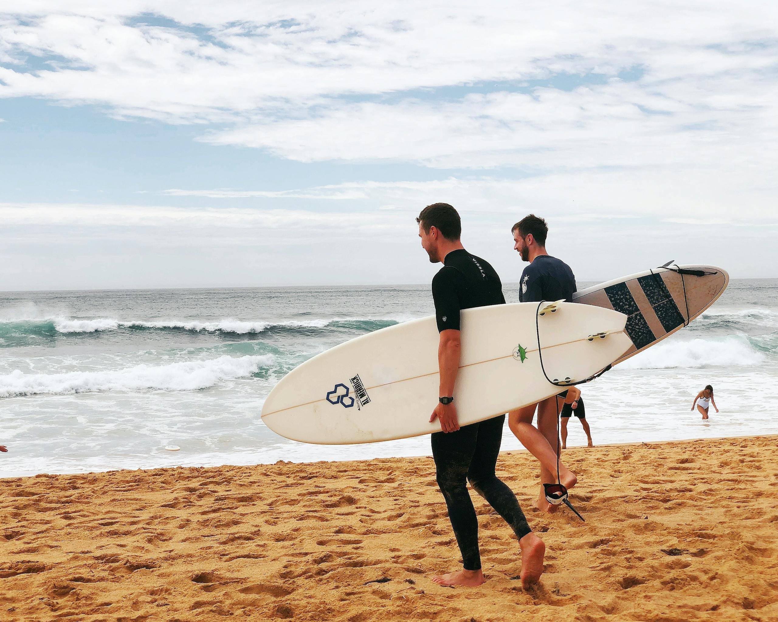 Two men with surfboards walking along Avoca Beach, NSW, capturing the essence of a summer day on the Australian coast.